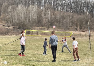 Children and young adults play volleyball on a meadow