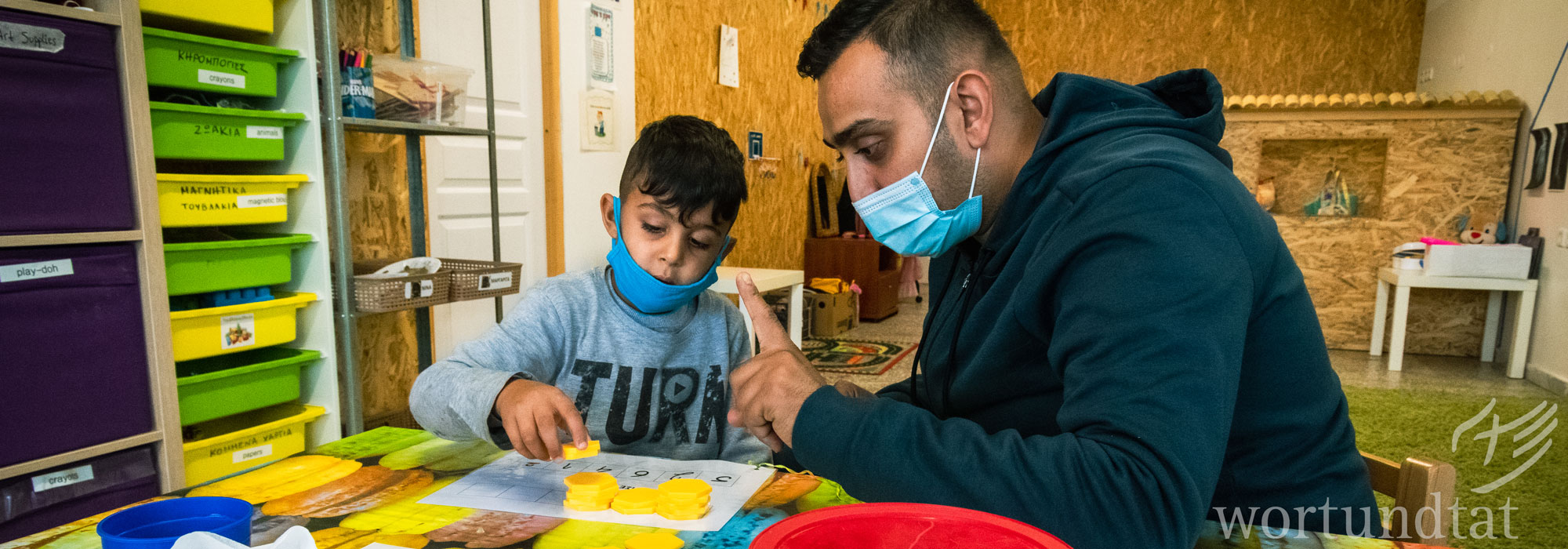 Mann zeigt Roma-Jungen, wie er mit Plättchen richtig zählen lernt.