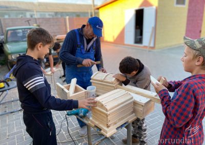 Man and three boys build wooden boxes together